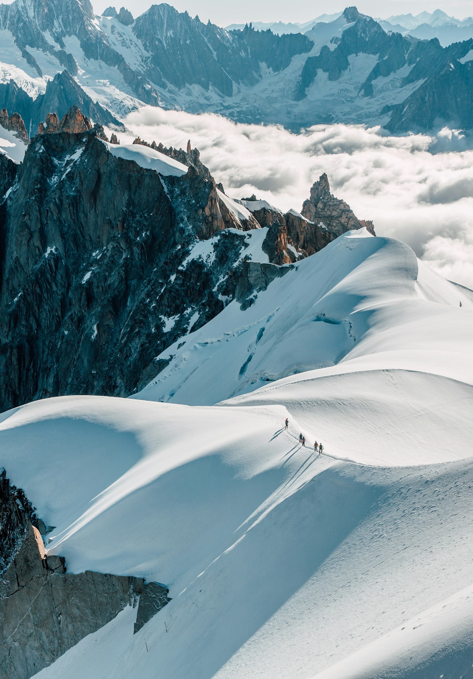 Roped mountaineers crossing a snow ridge above the clouds near Chamonix